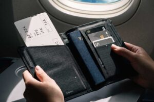 飛行機の窓際の座席で、パスポートと搭乗券を収納したbitplay スリム・バイフォールド パスポートホルダーを開いている様子