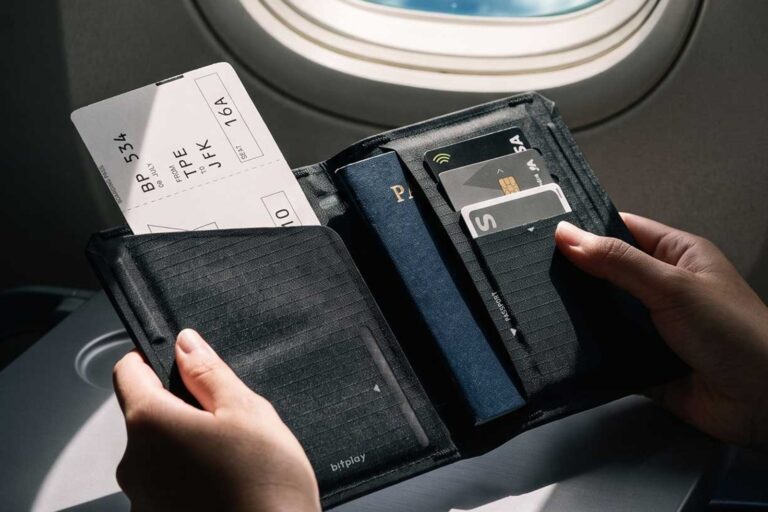 飛行機の窓際の座席で、パスポートと搭乗券を収納したbitplay スリム・バイフォールド パスポートホルダーを開いている様子